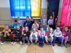 Uczestnicy zajęć plastycznych siedząc na materacach trzymają w dłoniach wykonane przez siebie kwiaty z bibuły.